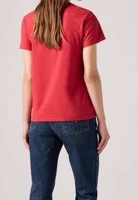 T-shirt rouge en coton à manches courtes avec une coupe décontractée, associée à un jean en denim bleu foncé avec des poches arrière et une texture subtile.