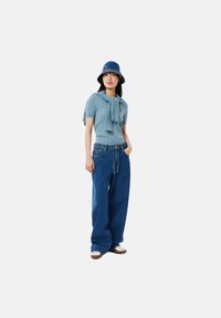 Top de punto azul claro con mangas cortas, acompañado de jeans de mezclilla azul de pierna ancha. Llevado con un sombrero de cubo azul y zapatos casuales.
