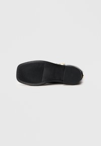 Sole di scarpa nera piatta con grip testurizzato e logo del marchio visibile, fotografata su uno sfondo bianco uniforme.