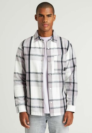 Camisa de franela gris y blanca a cuadros con botones a presión, un bolsillo en el pecho y líneas negras contrastantes. Textura suave, corte casual, mangas largas.