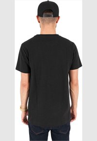 T-shirt noir à manches courtes avec un ourlet droit, texture douce, porté avec un jean foncé. La vue de dos montre un design simple et sans logo visible.