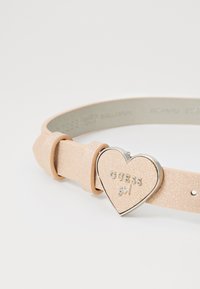 Rosa glitrende belte med et hjerteformet sølvspenne, preget med "GUESS girl." Har justerbar stropp med dobbel prong.