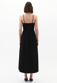 Schwarz ärmelloses Maxikleid mit gerafftem Oberteil, fließendem Rock und dünnen verstellbaren Trägern; glatte Textur und lockere Passform.