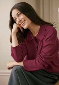 Pulover tricotat burgundy cu guler și detaliu cu nasturi, asortat cu o fustă gri. Textură moale și croială lejeră.