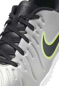 Scarpa da calcio sintetica grigia con lati testurizzati, accenti in pelle nera, lacci neri e un evidente logo Nike giallo neon.