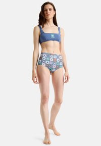 Top de bikini azul con escote cuadrado y tirantes anchos; la parte inferior de cintura alta presenta un patrón floral multicolor sobre un fondo azul claro.