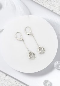 Silverörhängen med droppform har sammanflätade ringar med små ädelstenar, hängande från tunna kedjor och säkrade med fjäderlås.