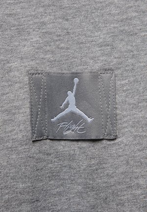 Gråt stof med en påsyet lap, der viser en silhuet af en basketballspiller, der hopper, og ordet "Flight" nedenfor.