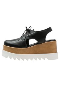 Chaussures à plateforme en cuir noir avec un design découpé, dotées d'une semelle en bois beige et d'une semelle blanche à bords dentelés. Fermeture à lacets, talon ouvert.