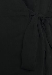 Tissu noir texturé noué de manière lâche avec des coutures visibles et de subtiles rainures verticales.