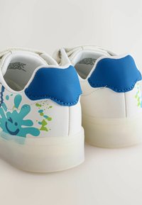 White sneakers with a blue textured heel tab and colorful splash designs in blue and green on the sides. Translucent rubber soles.