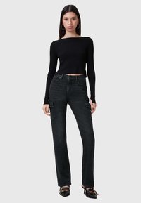 Top corto negro de manga larga con textura acanalada, combinado con pantalones cargo de mezclilla oscuros de tiro alto que cuentan con bolsillos laterales y pierna recta.