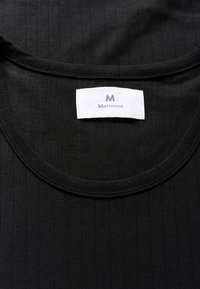 Juodas lygaus rašto megztinis T-shirt su apvalia iškirpte ir baltu ženklu, ant kurio parašyta „Matinique“ ir logotipas, esančiu prie iškirptės.