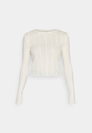 Balta ilga rankovė trumpa viršūnė su tekstūruotu mezgimo raštu, su grioveliais ir banginiais kraštais. Lengva ir prigludusi konstrukcija.