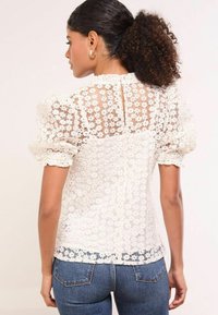 Weiße, durchsichtige Bluse mit floraler Spitzenüberlagerung, kurzärmeligen Puffärmeln und Rundhalsausschnitt mit einer kleinen Öffnung im Rücken und Zierdetails.