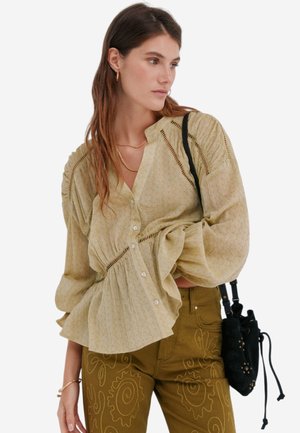 Lichtgele blouse met gathered mouwen en kantdetails, met een losse silhouet. Gecombineerd met olijfgroene broek met bloemenborduursel.