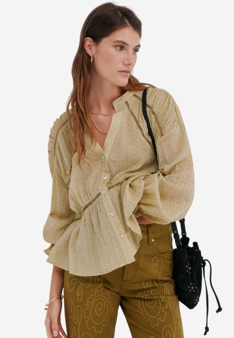 Lys gul bluse med samlede ærmer og blonder detaljer, som har en løs silhuet. Matchet med olivengrønne bukser med blomsterbroderi.