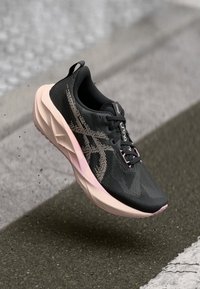 Zwarte hardloopschoen met roze accenten, gestructureerde bovenkant, gebogen zool en unieke patroon-details. Lichtgewicht ontwerp voor optimale prestaties.