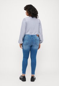 Gaiši pelēka blūze ar pūkainām piedurknēm, apvienota ar šaurām ziliem džinsiem ar izsistu apakšējo malu un aizmugurējām kabatām, valkāta ar masīviem melniem apaviem.