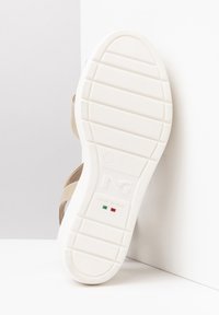 Sandale tan avec une tige en cuir beige et une semelle en caoutchouc blanche. Présente un fond plat avec des rainures texturées et une inscription "FABRIQUÉ EN ITALIE".