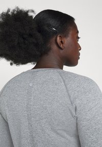 Gray athletic top with textured fabric and raglan sleeves. Features a small logo at the back and a smooth, clean design.