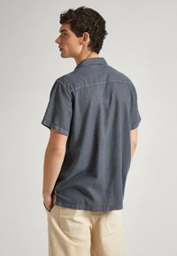 Men's short-sleeve shirt in dark gray cotton blend. Features a camp collar, straight hem, and subtle stitching detail across the back.