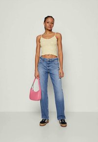 Top de tanque amarelo, curto e texturizado; jeans de cintura alta, desgastados e de cor azul clara; saco rosa; ténis plataforma preto e branco.