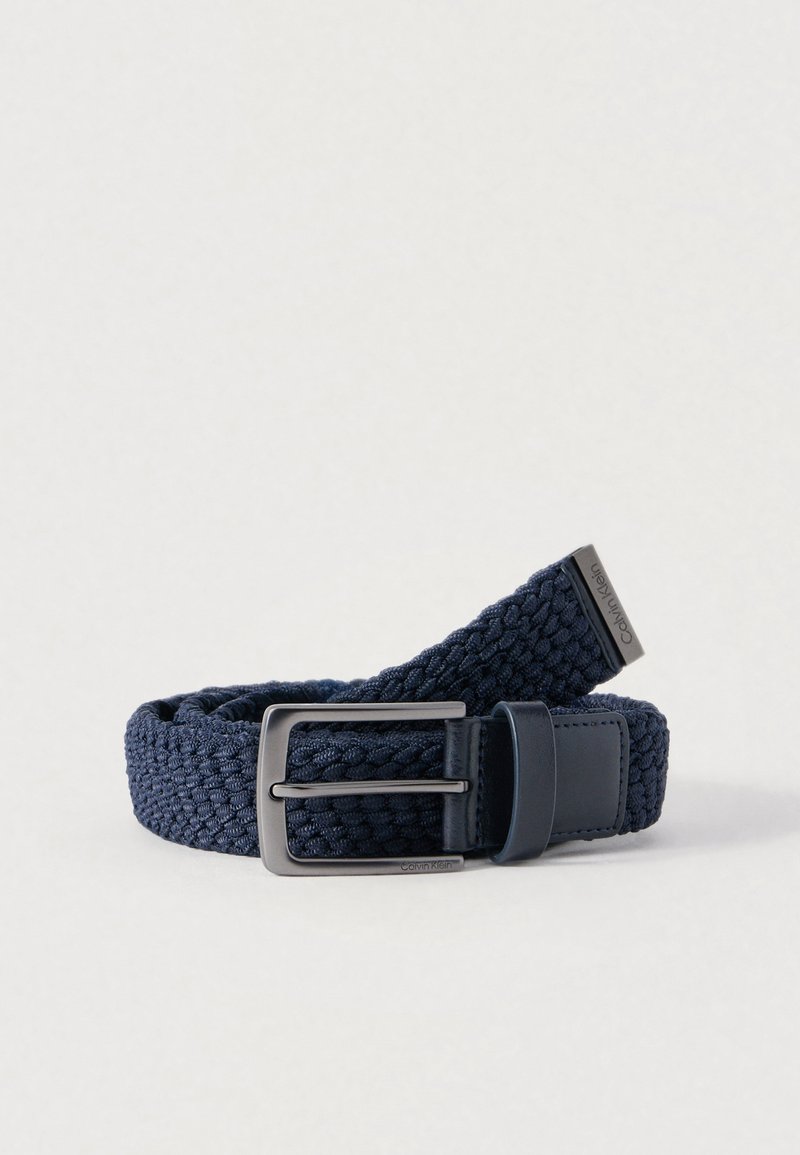 Ceinture tissée bleu marine en tissu élastique avec une boucle métallique argentée. Comprend des accents en cuir lisse et une finition texturée.