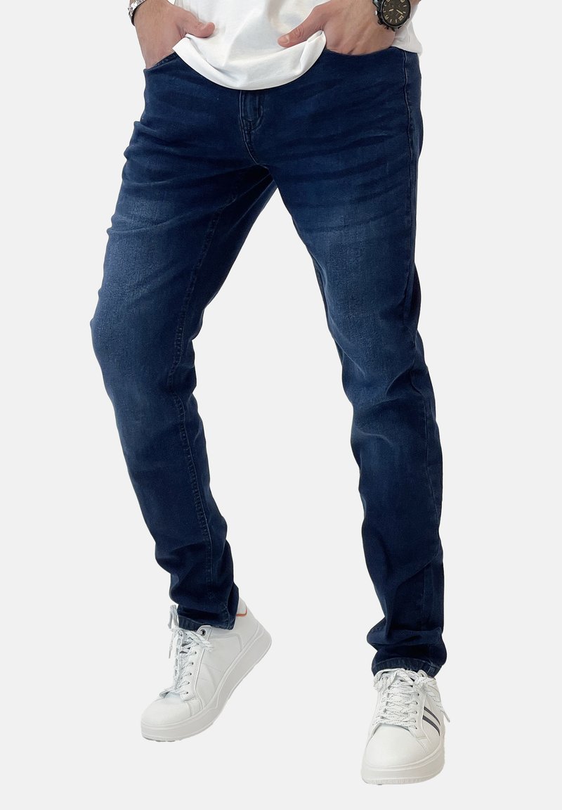 Vaqueros ajustados de color azul oscuro hechos de denim, con una textura suave y un ligero desgaste, combinados con zapatillas blancas.