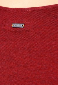 Burgunderfarbener Stricktop mit strukturiertem Finish und einem kleinen Metallschild mit der Aufschrift "BOSS ORANGE", das mit orangefarbenem Faden angenäht ist.