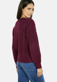 Maglione a maglia color vino con una vestibilità morbida, colletto e polsini a coste, abbinato a jeans in denim blu. La texture sembra morbida e leggermente pelosa.
