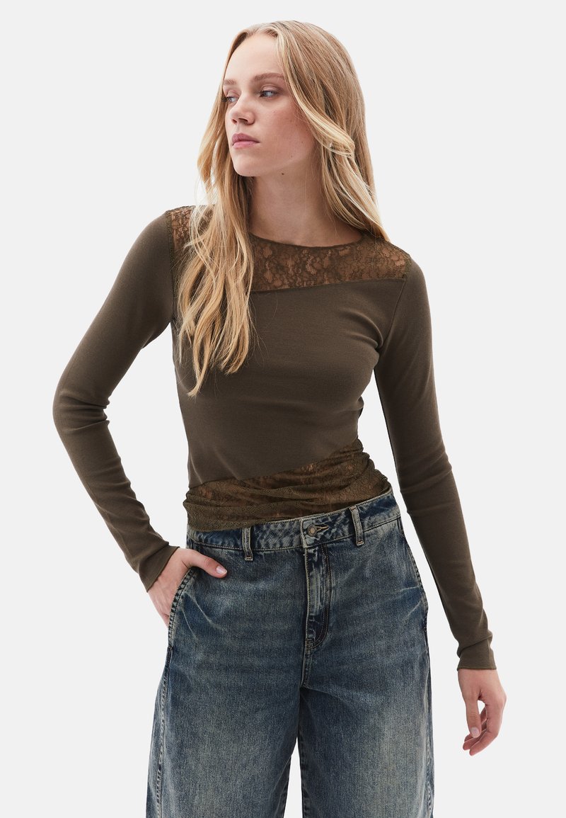 Olijfgroene longsleeve top met kantaccenten op de schouders en onderkant, gecombineerd met hoge taille, lichtblauwe denim jeans met een losse pasvorm.