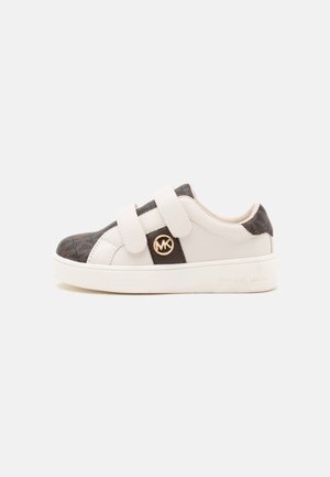 Baskets basses blanches et marron avec deux brides en velcro et un logo MK rond doré sur le côté, posées sur un fond uni.
