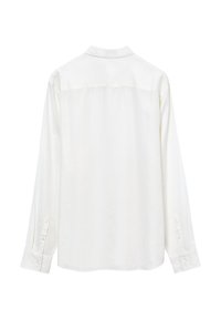 Camicetta bianca a maniche lunghe realizzata in tessuto morbido. Presenta un colletto classico, polsini con bottone e un orlo leggermente curvato. Design semplice sul retro.