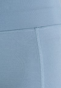 Tessuto attivo di colore blu chiaro con una consistenza liscia e dettagli di cucitura visibili lungo le cuciture, che mostrano un design sagomato.