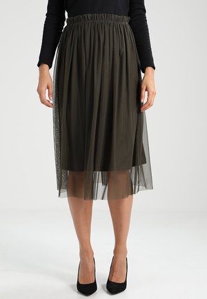 Grüne, plissierte Midirock mit einem transparenten Tüllüberzug, elastischem Bund und geschichteter Gestaltung. Trägt schwarze High Heels.