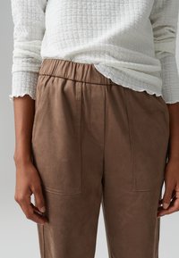 Brown suede pants with an elastic waistband and side pockets. Material has a soft, smooth texture, visible stitching detail.