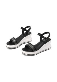 Sandali con zeppa nera, dotati di una cinghia lucida e di una fascia testurizzata. Presentano una piattaforma bianca con strisce nere e una cinghia alla caviglia regolabile.