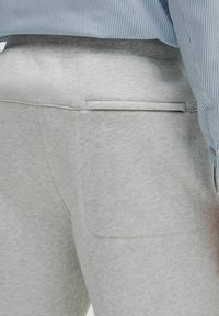 Grå sweatpants med en blød tekstur, der har en baglomme og en ribbet talje. Synlig stikninger fremhæver designet.