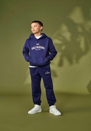 Marineblauwe hoodie met "ONLY&SONS" logo, gecombineerd met marineblauwe trainingsbroek. Model draagt witte sneakers. Soepele stof, casual pasvorm, geen patronen.