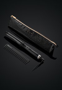 Fer à friser noir avec des accents argentés, accompagné d'un peigne noir et d'une trousse zippée noire texturée avec fermeture dorée, le tout sur une surface réfléchissante.