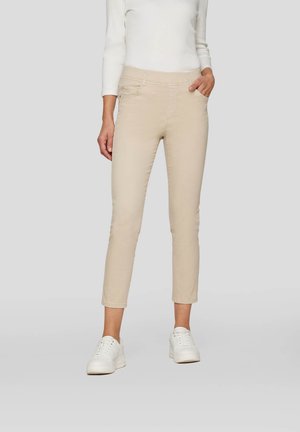 Beige cropped pants made of cotton with a smooth texture. Features a flat waistband and side pockets, paired with white sneakers.