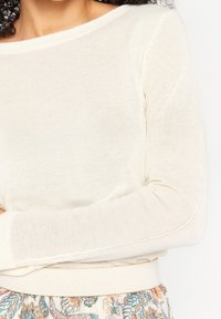 Kremowy sweter z dzianiny z długimi rękawami, okrągłym dekoltem i ściągaczami na mankietach, charakteryzujący się miękką fakturą i dopasowanym krojem.