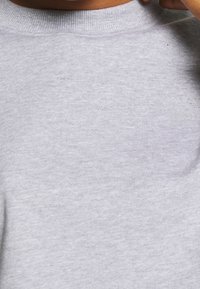 Harmaa puuvillainen crewneck-huppari, jossa on ribatty kaulaosa, ja jossa on hienovarainen bränditeksti rinnassa sekä pehmeä tekstuuri.