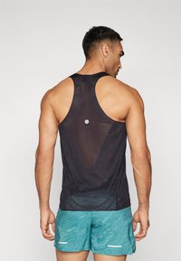 Débardeur de sport noir avec un dos en mesh, doté d'un détail réfléchissant rond, porté avec un short à motifs turquoise. Tissu lisse et design dos nageur.