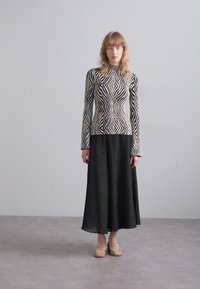 Langsleeve top met een zwart-wit zigzagpatroon, gecombineerd met een vloeiende zwarte geplooide rok; model draagt beige loafers.