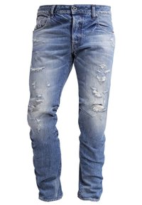Jeans de mezclilla azul con corte ajustado y múltiples áreas desgastadas y descoloridas en los muslos frontales y las rodillas.