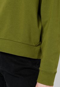 Sweat-shirt vert olive en tissu doux, avec ourlet et poignets côtelés, coupe décontractée et texture lisse. Les détails mettent l'accent sur le confort.