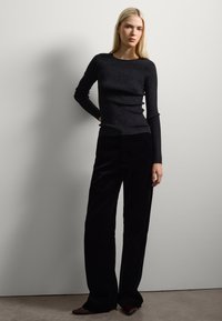 Zwarte fitted longsleeve top met een textuurpatroon, gecombineerd met hooggetailleerde zwarte fluwelen broek met brede pijpen. Puntige schoenen in donker bordeaux.