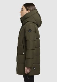 Geacă puffer de culoare verde măslin, cu o glugă mare, design matlasat, nasturi negri, buzunare cu fermoar și branding pe margine și pe mânecă.